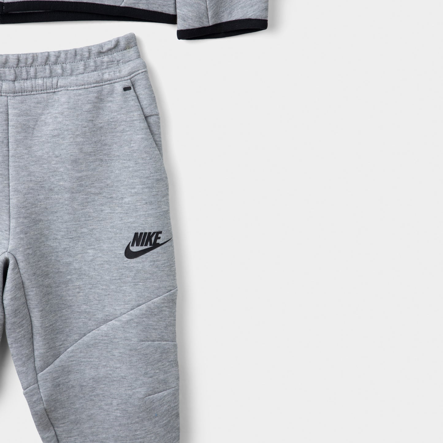 Nike Sportswear Children's Tech Fleece Full Zip Hoodie Set. Close-up of dark grey heather joggers showing the elastic waistband, black Nike logo and tapered leg.