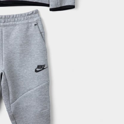 Nike Sportswear Children's Tech Fleece Full Zip Hoodie Set. Close-up of dark grey heather joggers showing the elastic waistband, black Nike logo and tapered leg.