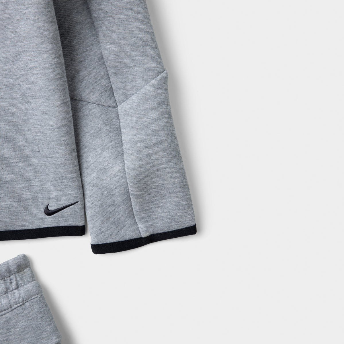 Nike Sportswear Children's Tech Fleece Full Zip Hoodie Set. Close-up of dark grey heather hoodie showing the sleeve, black Nike Swoosh and contrast trim.