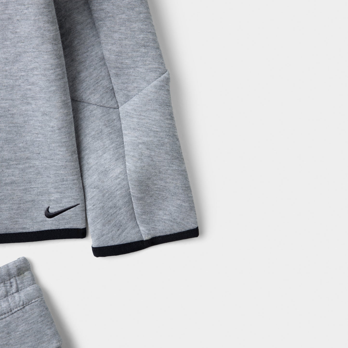Nike Sportswear Children's Tech Fleece Full Zip Hoodie Set. Close-up of dark grey heather hoodie showing the sleeve, black Nike Swoosh and contrast trim.