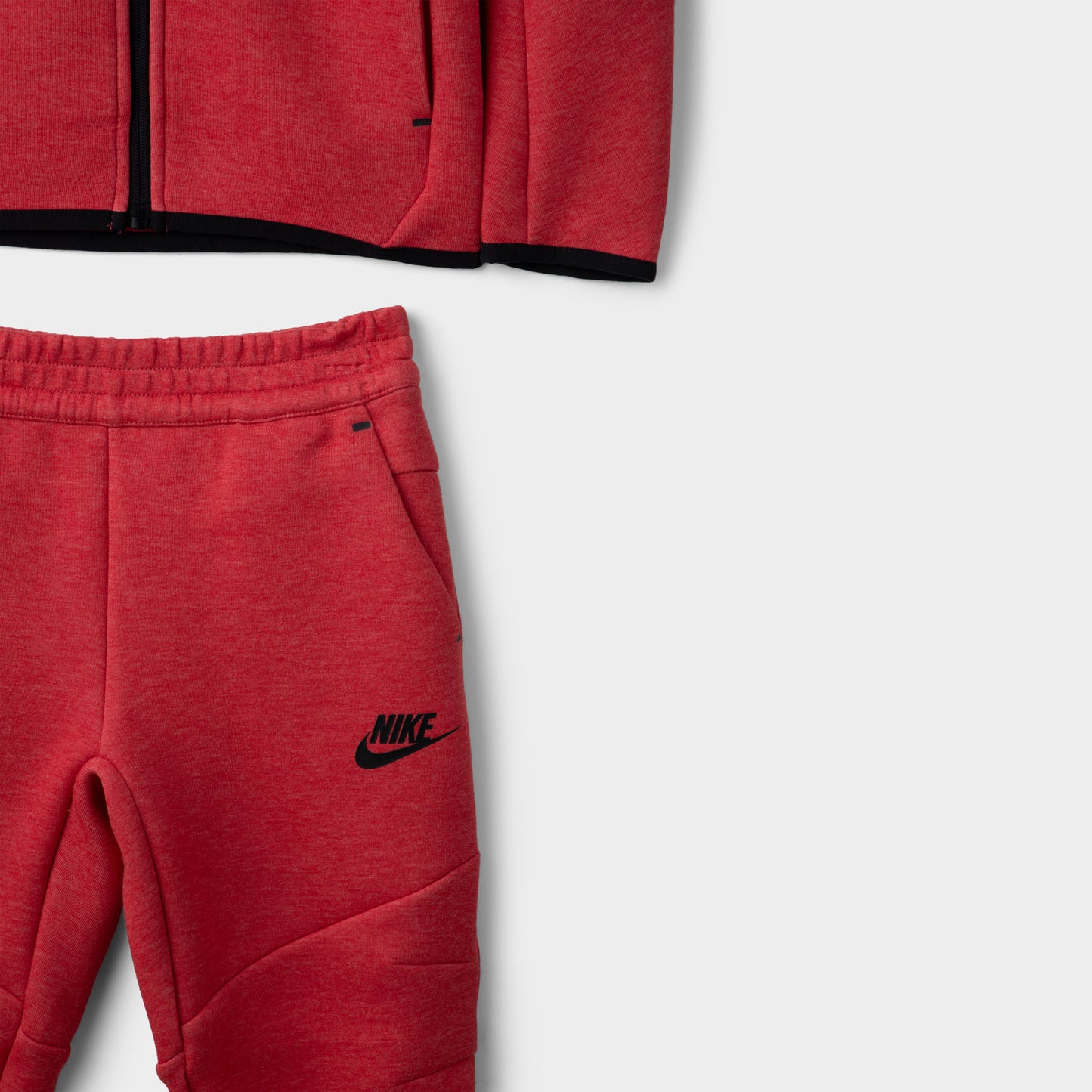 Nike Children's Sportswear Tech Fleece Full Zip Hoodie Set. Close-up of light university red and heather joggers showing elastic waistband, tapered legs and black Nike branding.