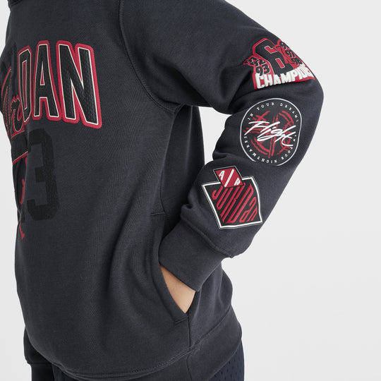 Jordan Juniors' Varsity Split Pullover Hoodie. Close-up of off noir hoodie showing gym red Jordan lettering, sleeve patches and ribbed cuff.