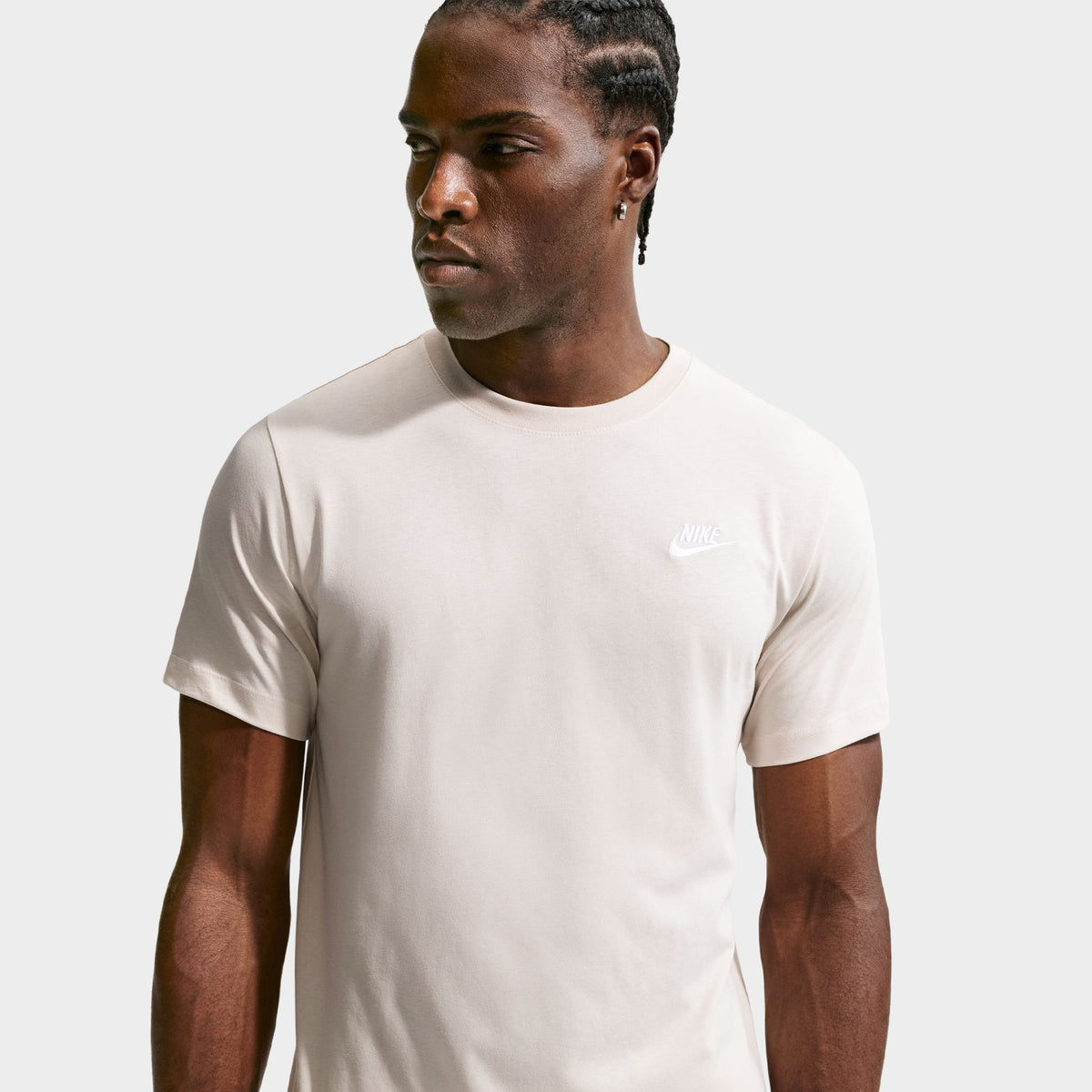 Nike Sportswear Club Tee. Front close-up of model wearing light orewood brown T-shirt with crew neckline, short sleeves and small white Nike Swoosh on the chest.