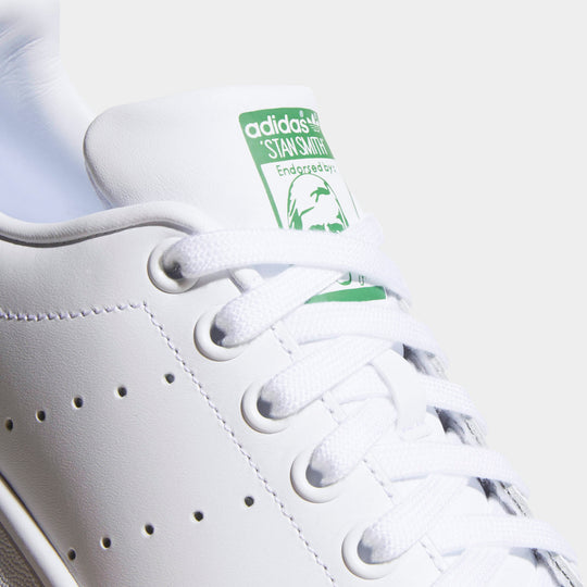 adidas Women's Stan Smith. Close-up of white and green sneaker showing white laces, perforated side panels and green tongue branding.