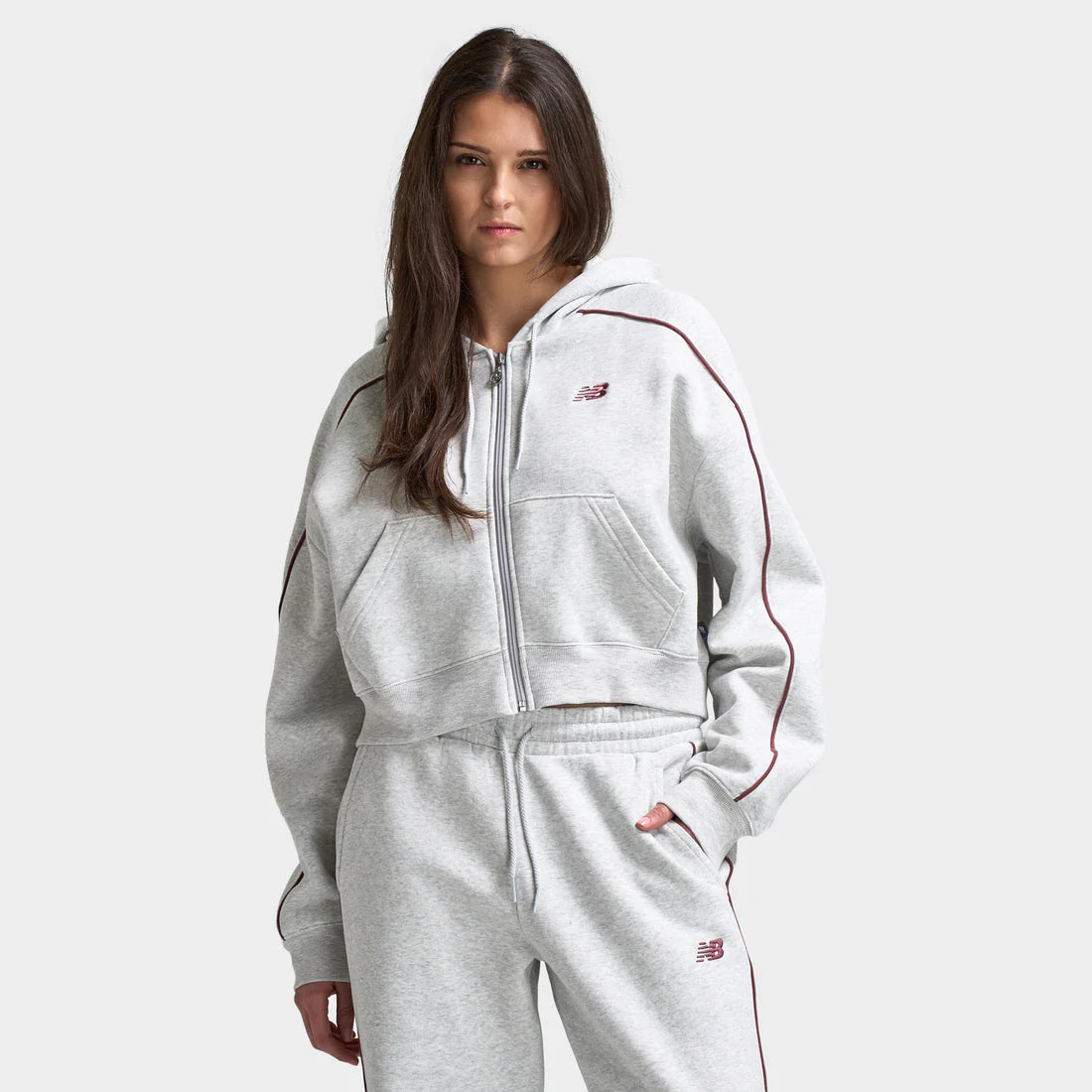 Woman wears New Balance Women’s Piping Fullzip Crop Hoodie “Grey” hoodie. Shop Women’s Clothing now at JD Sports.