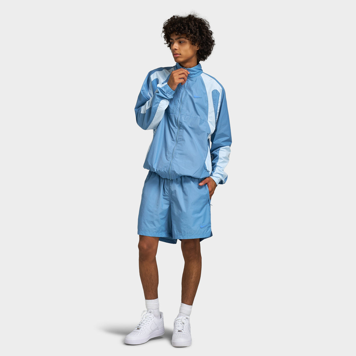 Nike NOCTA Cardinal Nylon Shorts. Full-length front model view styled with matching work blue track jacket. 