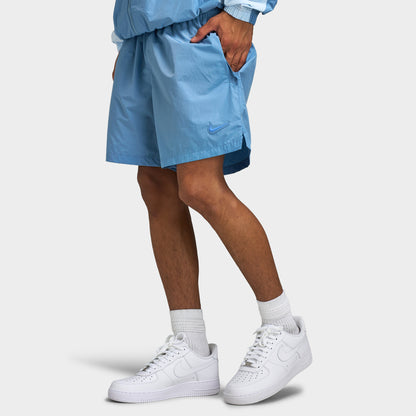 Nike Nike NOCTA Cardinal Nylon Shorts. Side profile lower body model view showing work blue nylon shorts, hand in pocket, above-the-knee length, and side notch hem detail.