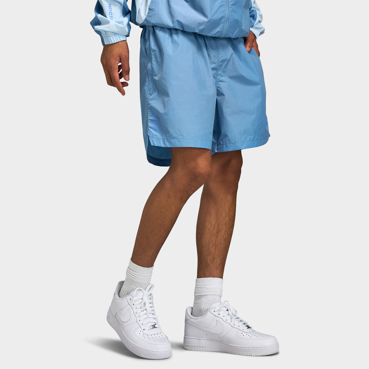 Nike NOCTA Cardinal Nylon Shorts. Three-quarter lower body model view displaying work blue nylon shorts, elastic waistband, and relaxed leg. 