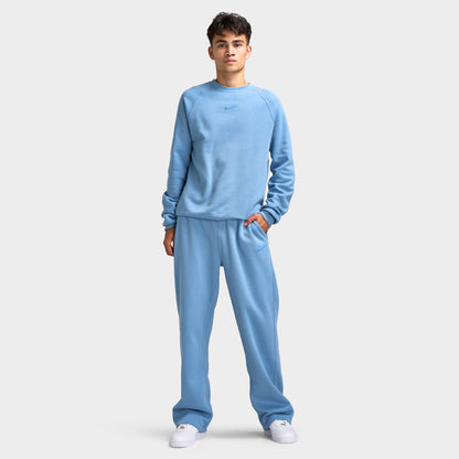 Nike NOCTA Fleece Open Hem Pants. Full-body view of model wearing work blue sweatpants with matching sweatshirt and white sneakers.