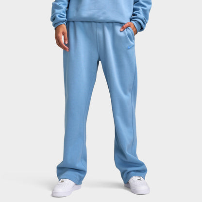 Nike NOCTA Fleece Open Hem Pants. Front view of model wearing work blue sweatpants with wide legs, elastic waistband and side pockets.