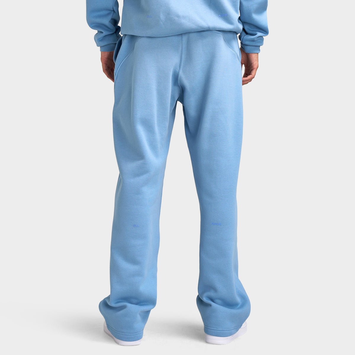 Nike NOCTA Fleece Open Hem Pants. Back view of model wearing work blue sweatpants with relaxed legs and open hems.
