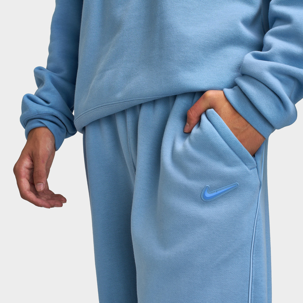 Nike NOCTA Fleece Open Hem Pants. Close-up of work blue sweatpants showing elastic waistband, side pocket and smooth fleece fabric.