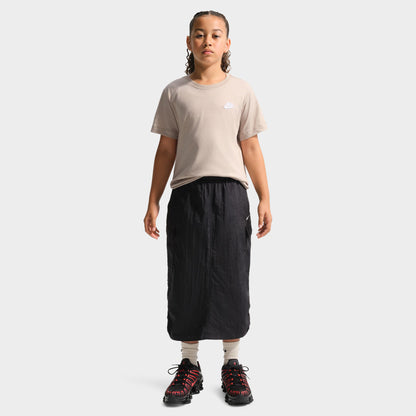 Nike Juniors' Futura T-Shirt. Full-length front view of a youth model wearing the moon particle beige shortsleeve t-shirt paired with a black skirt, showing the relaxed fit and straight hemline.