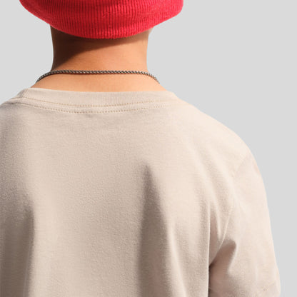 Nike Juniors' Futura T-Shirt. Close-up rear angle focusing on the smooth moon particle beige cotton fabric, ribbed crewneck collar construction, and shoulder seam detail.