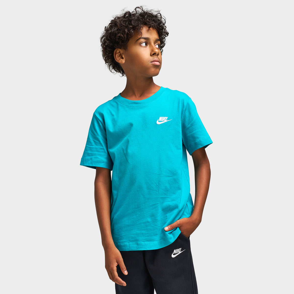 Nike Juniors' Futura T-Shirt. Upper body front model view of energy green turquoise cotton shortsleeve t-shirt featuring a ribbed crewneck, white Nike Futura logo with Swoosh on the left chest, straight hem, and standard fit.