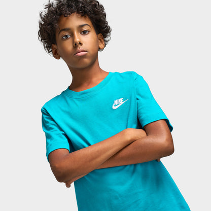 Nike Juniors' Futura T-Shirt. Three-quarter upper body model view displaying energy green turquoise shortsleeve t-shirt with arms crossed, ribbed crew collar, and white embroidered Nike Futura chest logo. 