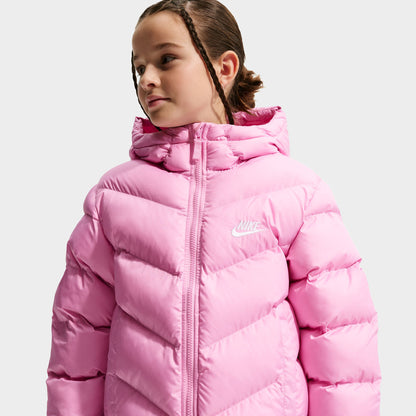 Nike Junior Girls' Therma-FIT Loose-Fit Puffer Jacket. Three-quarter view of model wearing pink rise puffer jacket with hood, zip closure and quilted sleeves.