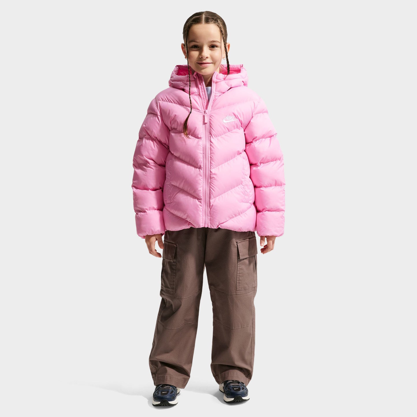 Nike Junior Girls' Therma-FIT Loose-Fit Puffer Jacket. Full-body view of model wearing pink rise puffer jacket with hood, quilted panels and front zip closure.
