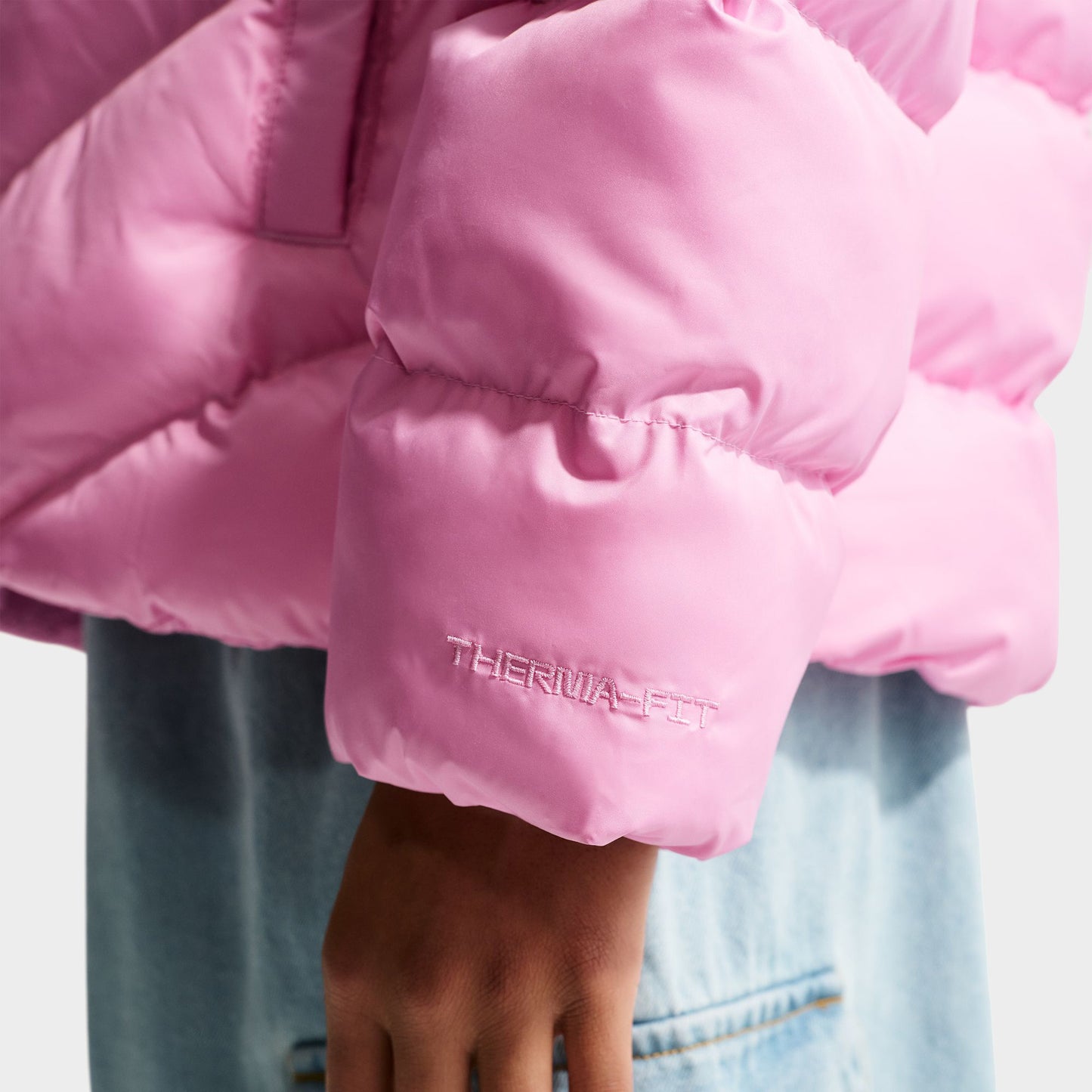 Nike Junior Girls' Therma-FIT Loose-Fit Puffer Jacket. Close-up of pink rise puffer jacket showing quilted sleeve, elastic cuff and padded construction.
