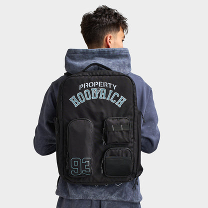 Hoodrich Varso Backpack. Back view of model wearing black backpack showing the structured shape, multiple zip compartments and large graphic branding.