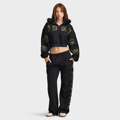 Hoodrich Women's Camo Rift Boxy Zip-Through Hoodie. Full-length front view of the model wearing the black cropped camo zip-through hoodie paired with matching black track pants. 
