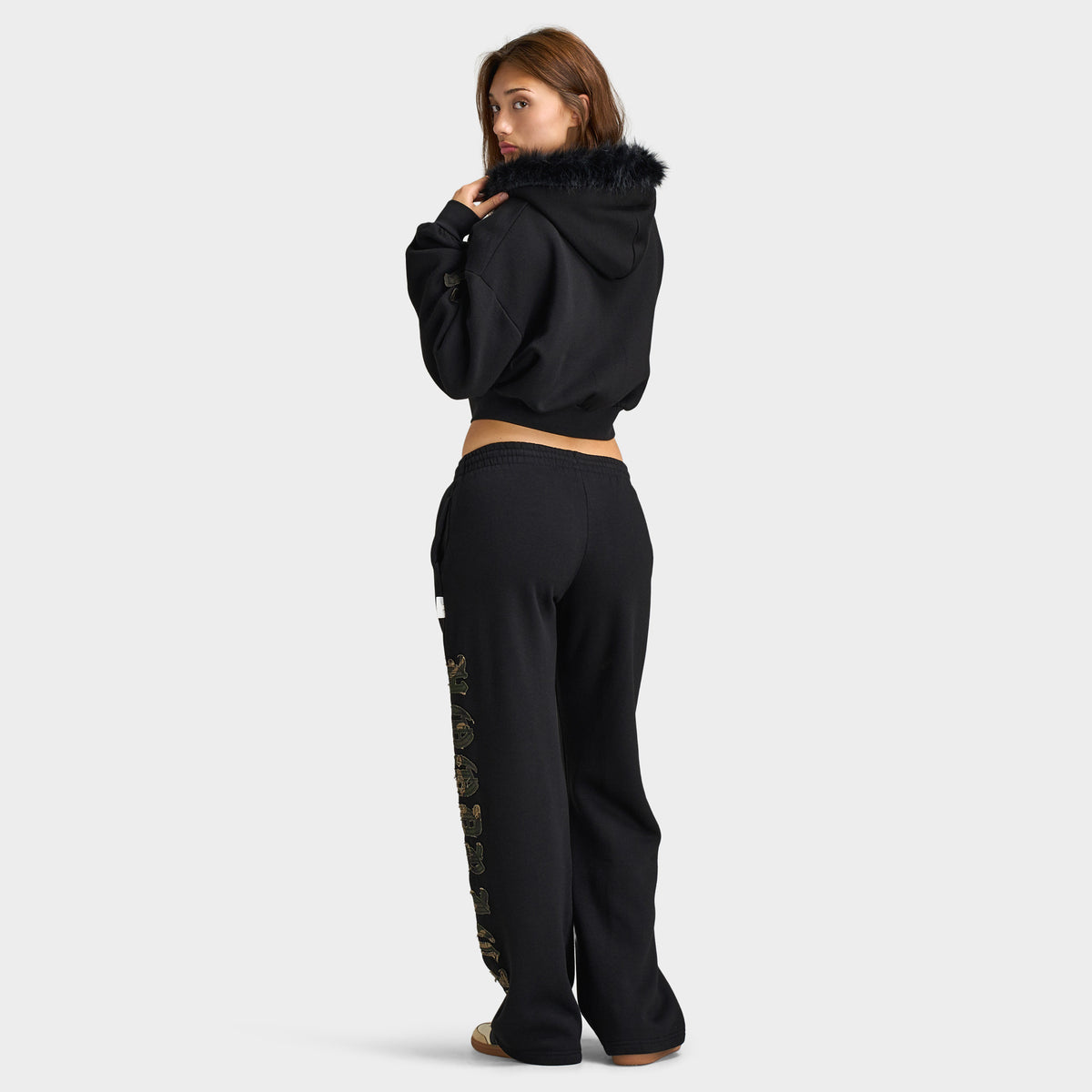 Hoodrich Women's Camo Rift Boxy Zip-Through Hoodie. Full-length three-quarter back view showing the cropped silhouette of the black hoodie paired with matching black sweatpants. 