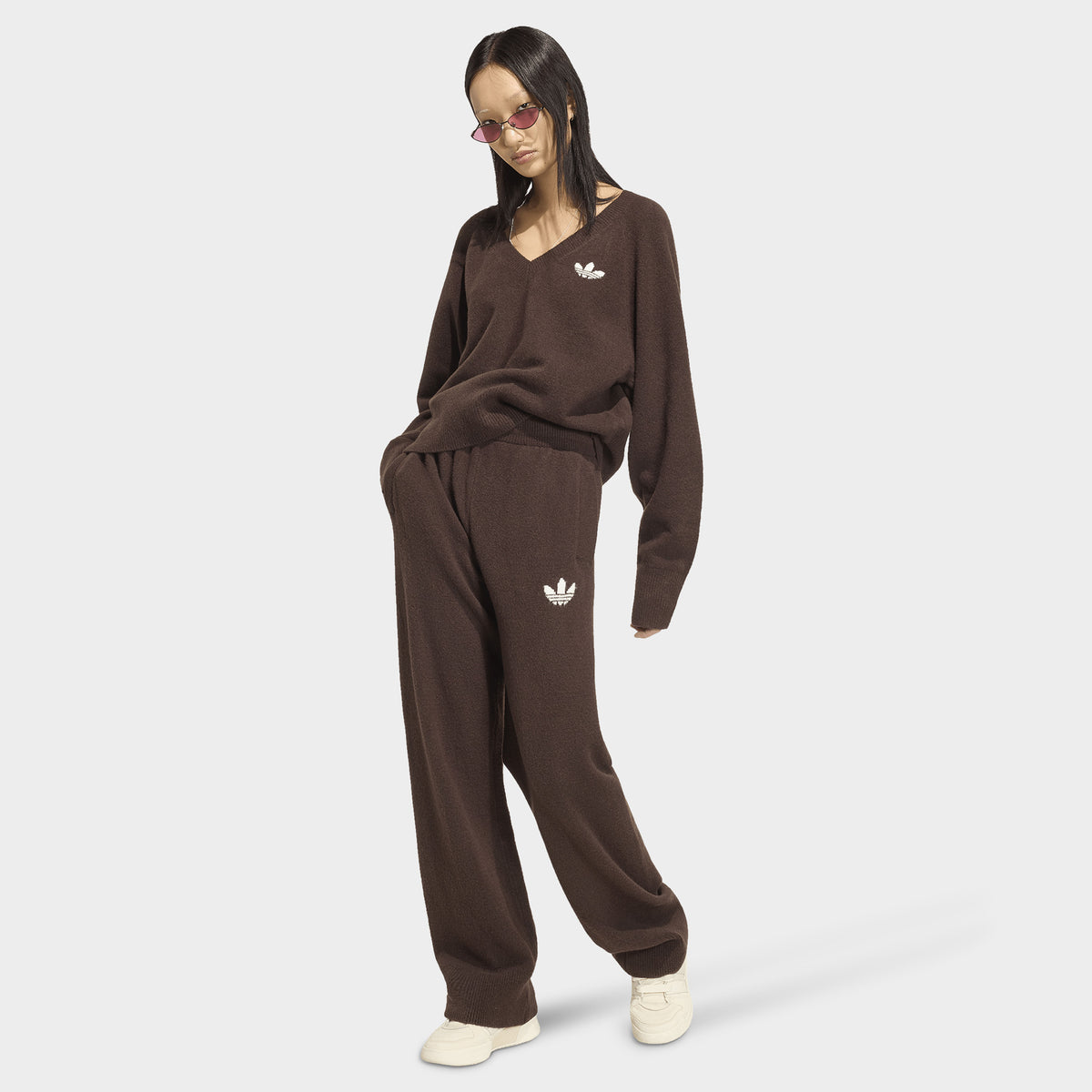 adidas Essentials Knit Pant. Full-body view of model wearing aurora coffee pants with matching top and light-coloured shoes.