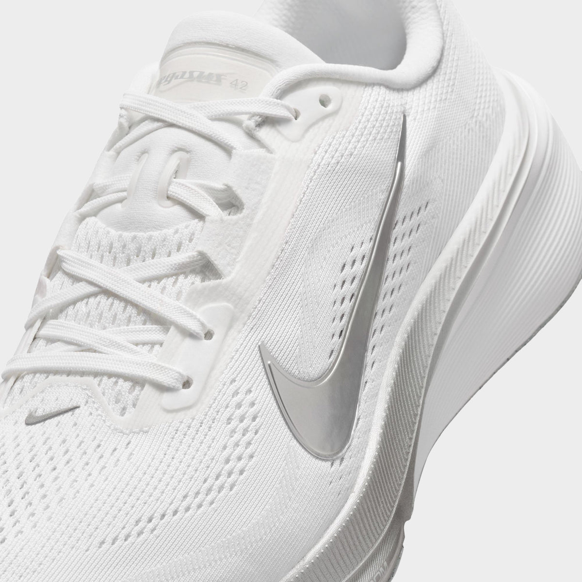 Nike Women's Pegasus 42. Close-up of white, metallic silver and wolf grey running shoe showing white laces, mesh panels and silver Swoosh.
