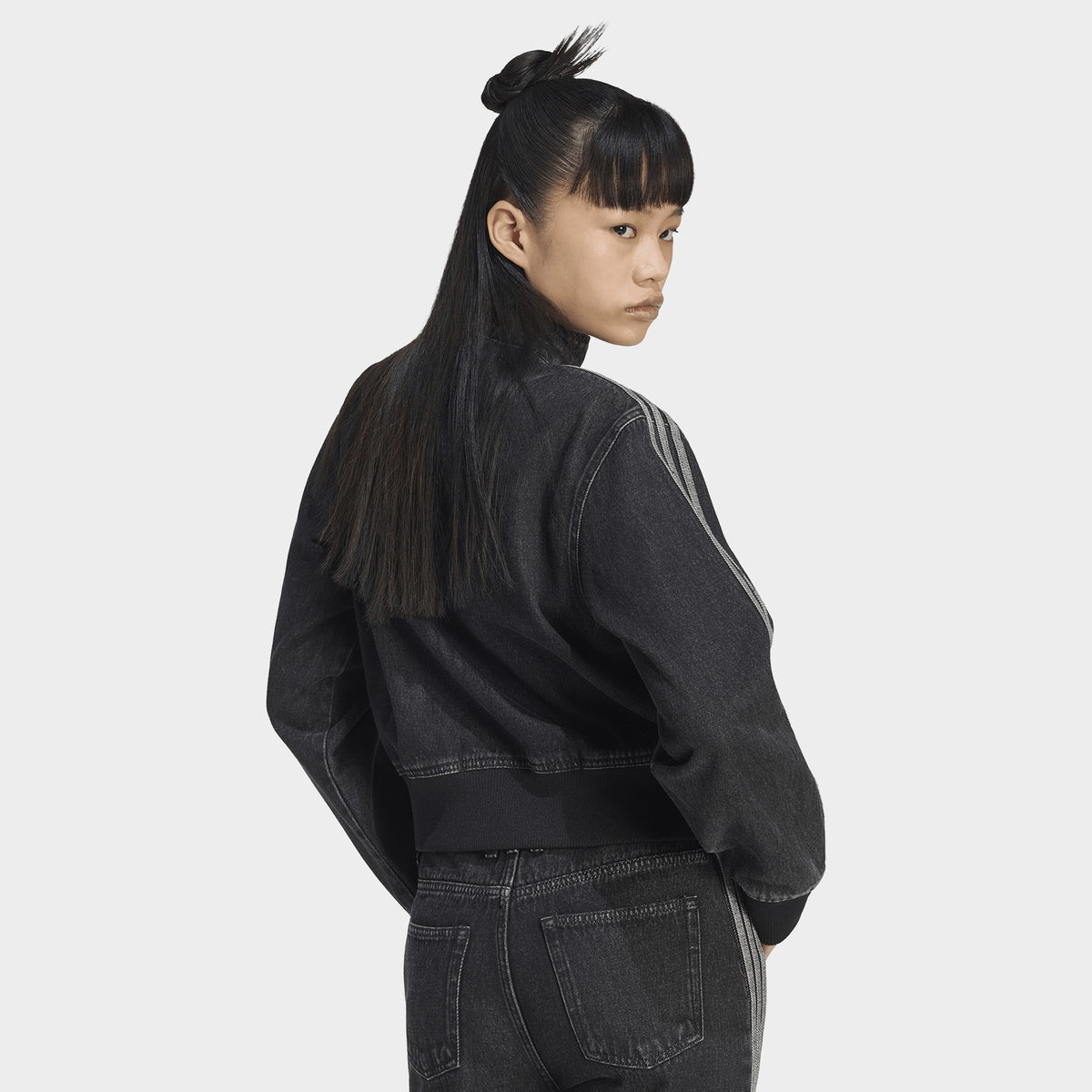 adidas Firebird Denim Track Top. Back three-quarter view of model wearing true black denim track jacket with plain back, high collar and relaxed sleeves.