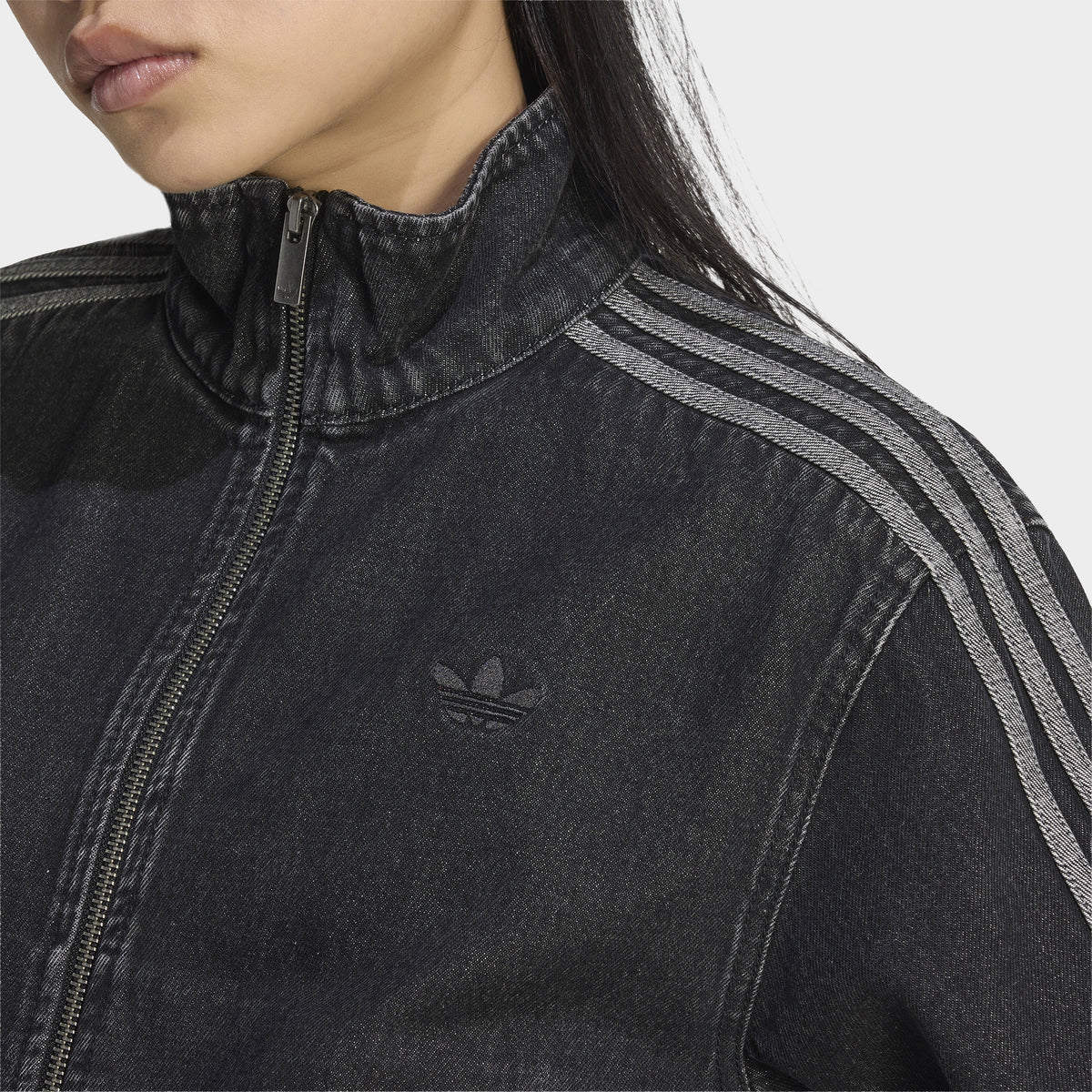 adidas Firebird Denim Track Top. Close-up of true black denim track jacket showing high collar, full-zip closure, contrast stitching and tonal three stripes.