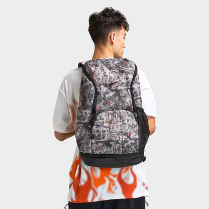 Nike Varsity Elite Backpack. Back view of model wearing cream and black backpack showing the all-over print, padded shoulder straps and top carry handle.