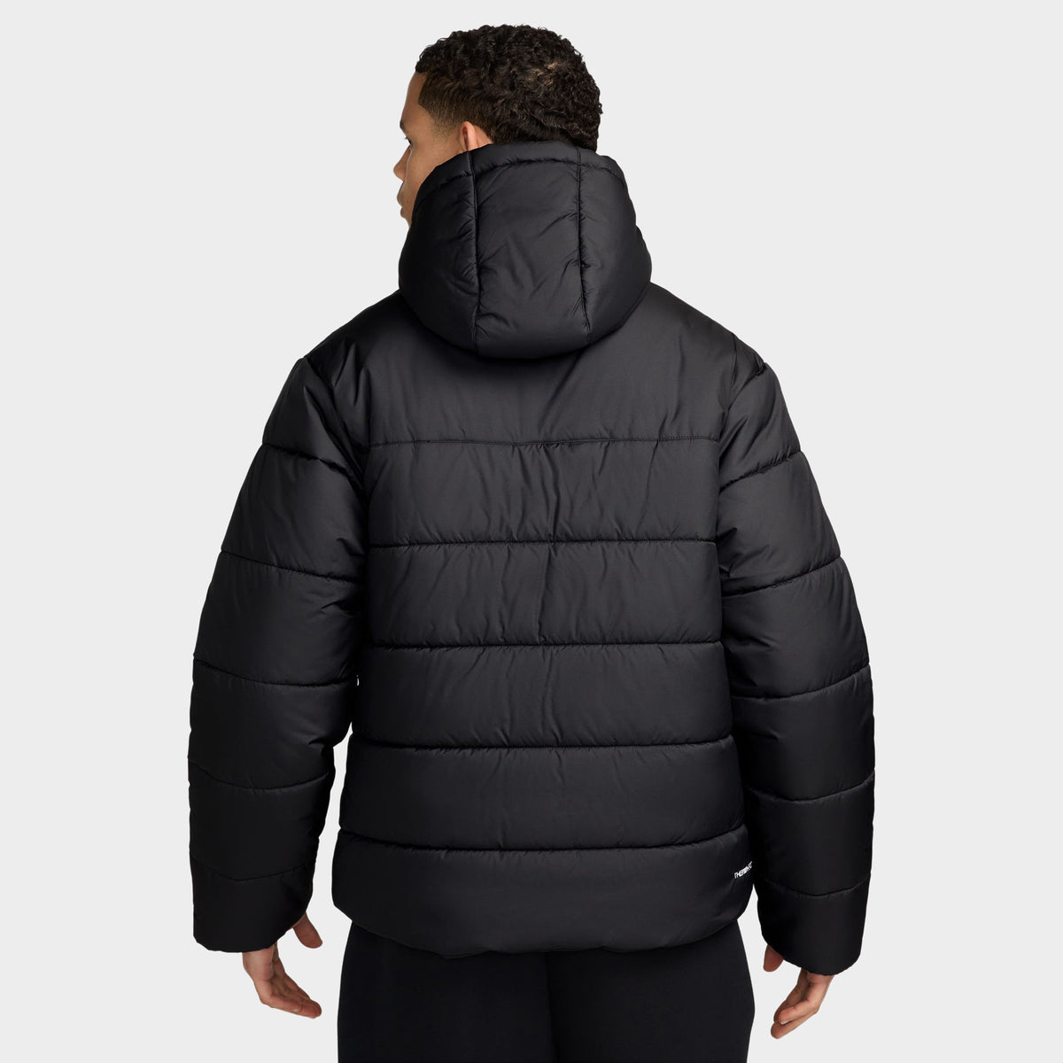 Nike Access Filled Puffer. Back view of model wearing black puffer jacket with hood, horizontal quilting and straight hem.