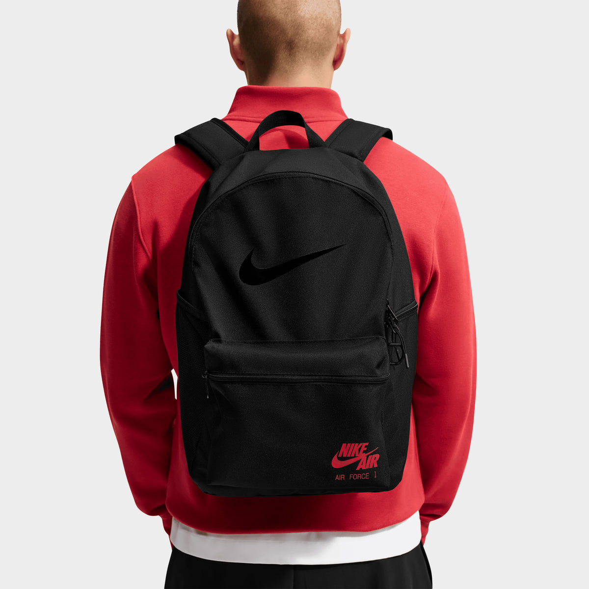 Nike AF1 Heritage Backpack. Back view of model wearing black backpack with padded shoulder straps and red Nike branding.