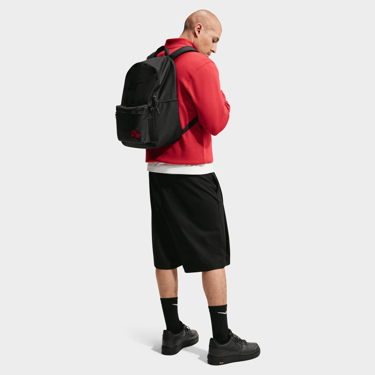 Nike AF1 Heritage Backpack. Back view of model wearing black backpack with padded shoulder straps and red Nike branding.