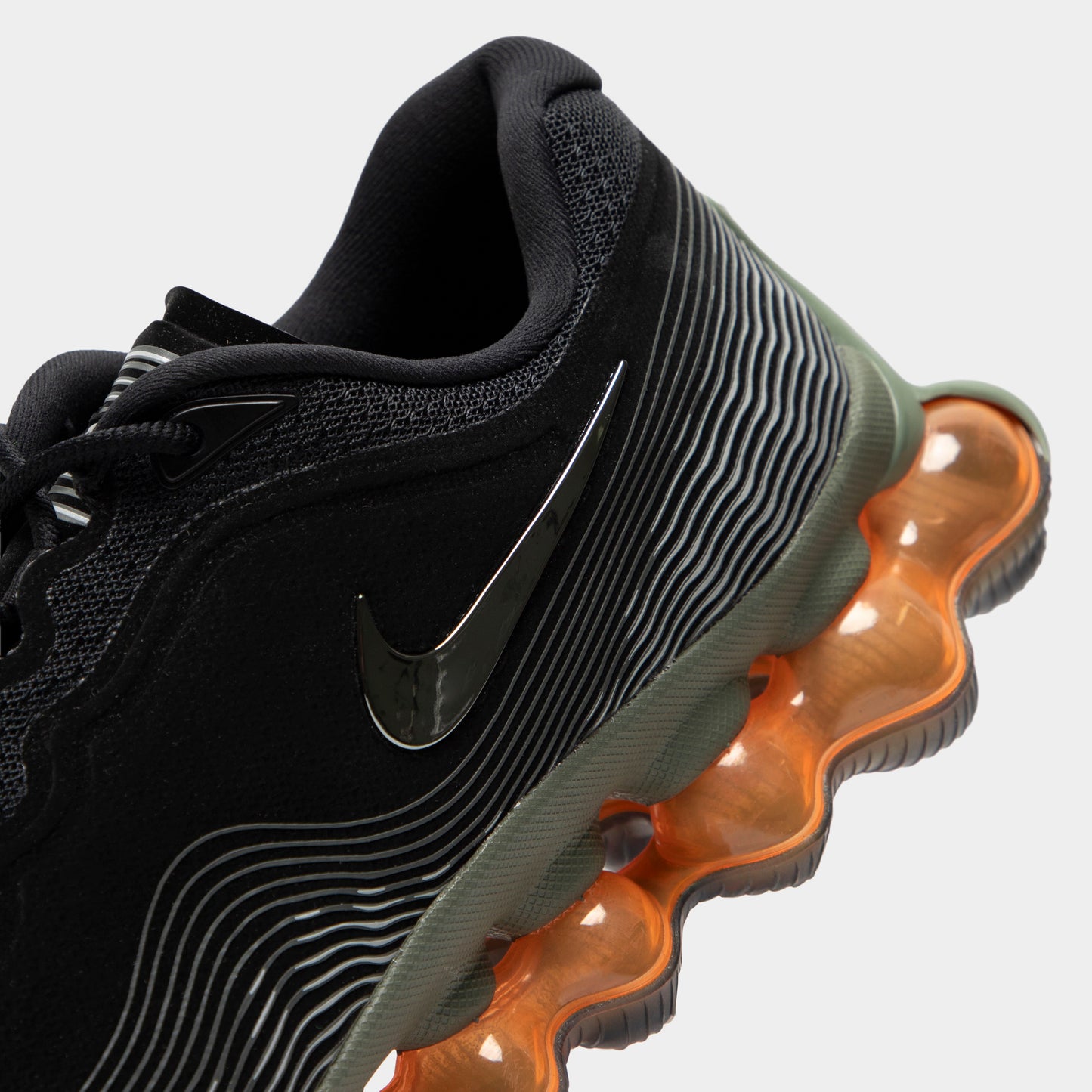 Nike Air Liquid Max. Close-up of black, metallic silver and light army sneaker showing black Swoosh, ribbed upper texture and amber Air cushioning pods.