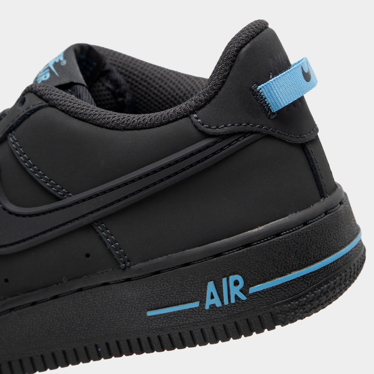 Nike Air Force 1 GS. Close-up view of lateral heel highlighting anthracite leather overlays, football blue heel pull tab, stitched midsole, and blue AIR branding. 