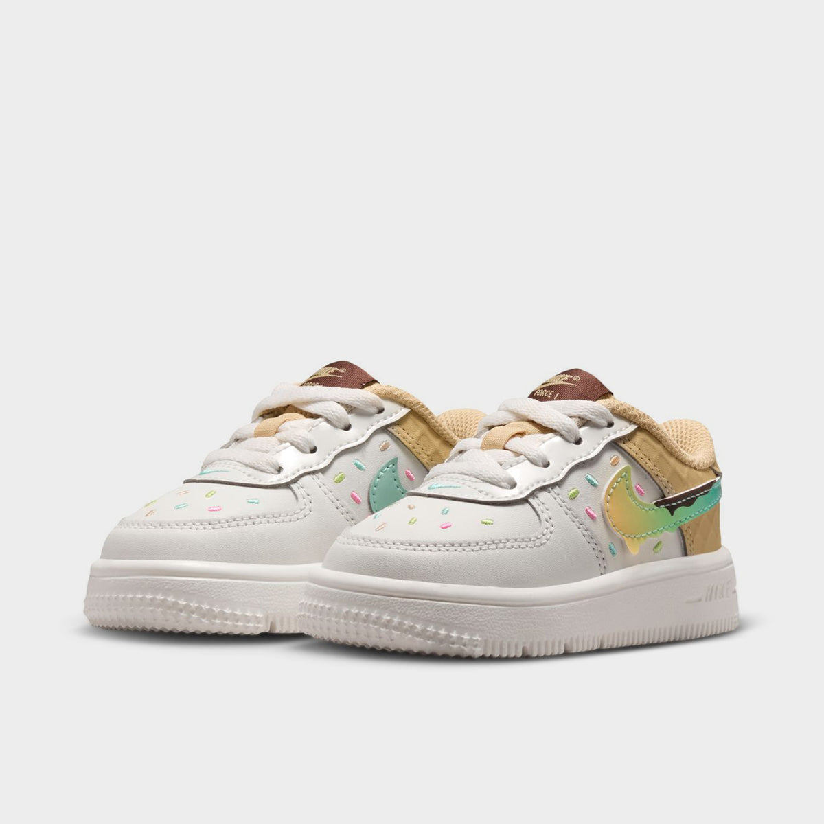 Nike Air Force 1 TD. Three-quarter view of sail, multicolour and sesame toddler sneakers with white laces, pastel Swooshes, brown tongue labels and white soles.