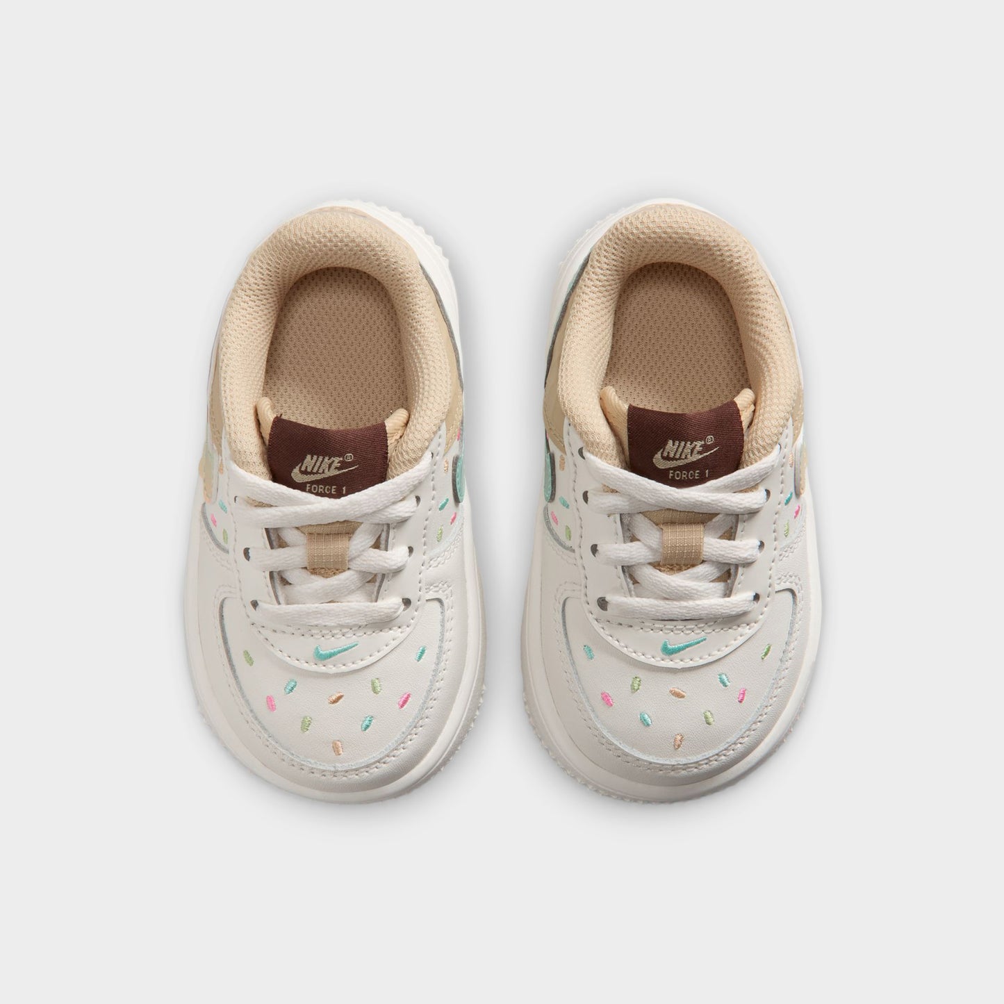 Nike Air Force 1 TD. Top view of sail, multicolour and sesame toddler sneakers showing white laces, brown tongue labels and beige collars.