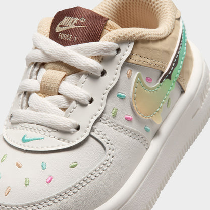 Nike Air Force 1 TD. Close-up of sail, multicolour and sesame toddler sneaker showing white laces, brown tongue label, pastel Swoosh and colourful perforations.