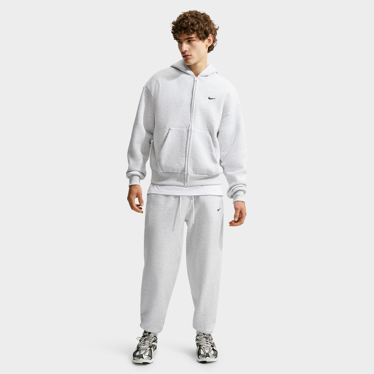 Nike Solo Fleece Full-Zip Hoodie. Full-length front view of model wearing birch heather full-zip hoodie styled with matching grey fleece pants and sneakers. 