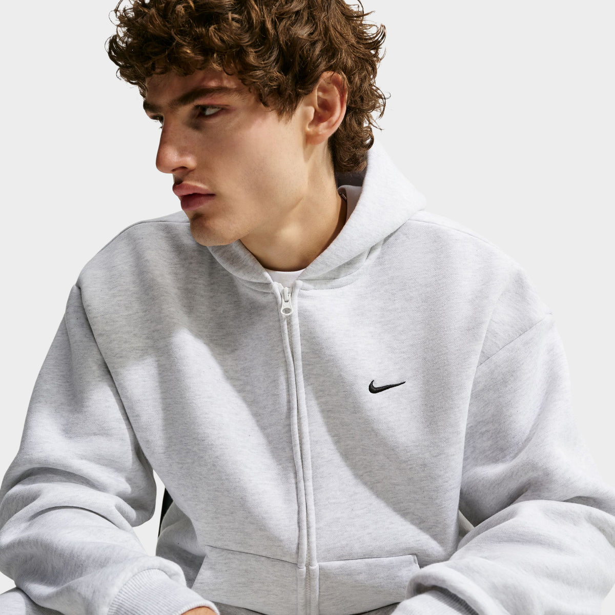 Nike Solo Fleece Full-Zip Hoodie. Angled front view highlighting full zip front, lined fleece hood, dropped shoulder seams, and small black Swoosh logo. 