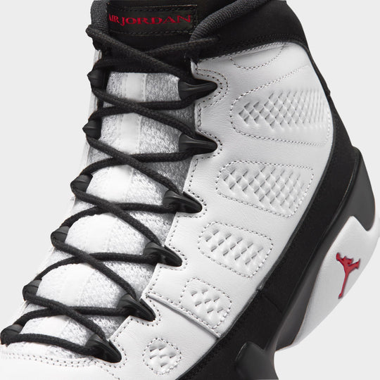 Jordan 9 Retro. Close-up view of upper highlighting white perforated leather side panel, black plastic speed lacing loops, black round laces, white tongue, and black collar trim with true red "AIR JORDAN" tongue detailing. 