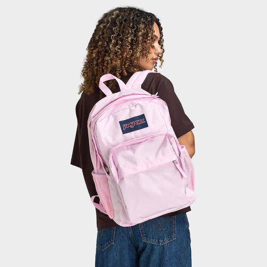 JanSport Big Plans Backpack. Side view of model wearing pink backpack with adjustable shoulder straps, front pocket and top carry handle.