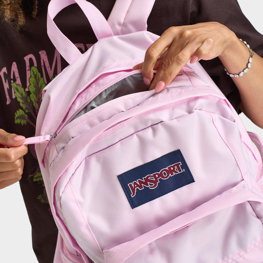 JanSport Big Plans Backpack. Close-up of pink backpack showing front zip pocket, JanSport logo patch, zipper pulls and top handle.