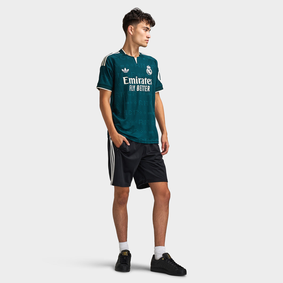 adidas Real Madrid Away Jersey. Full-body front view of model wearing aurora ivy soccer jersey with black shorts and dark shoes.