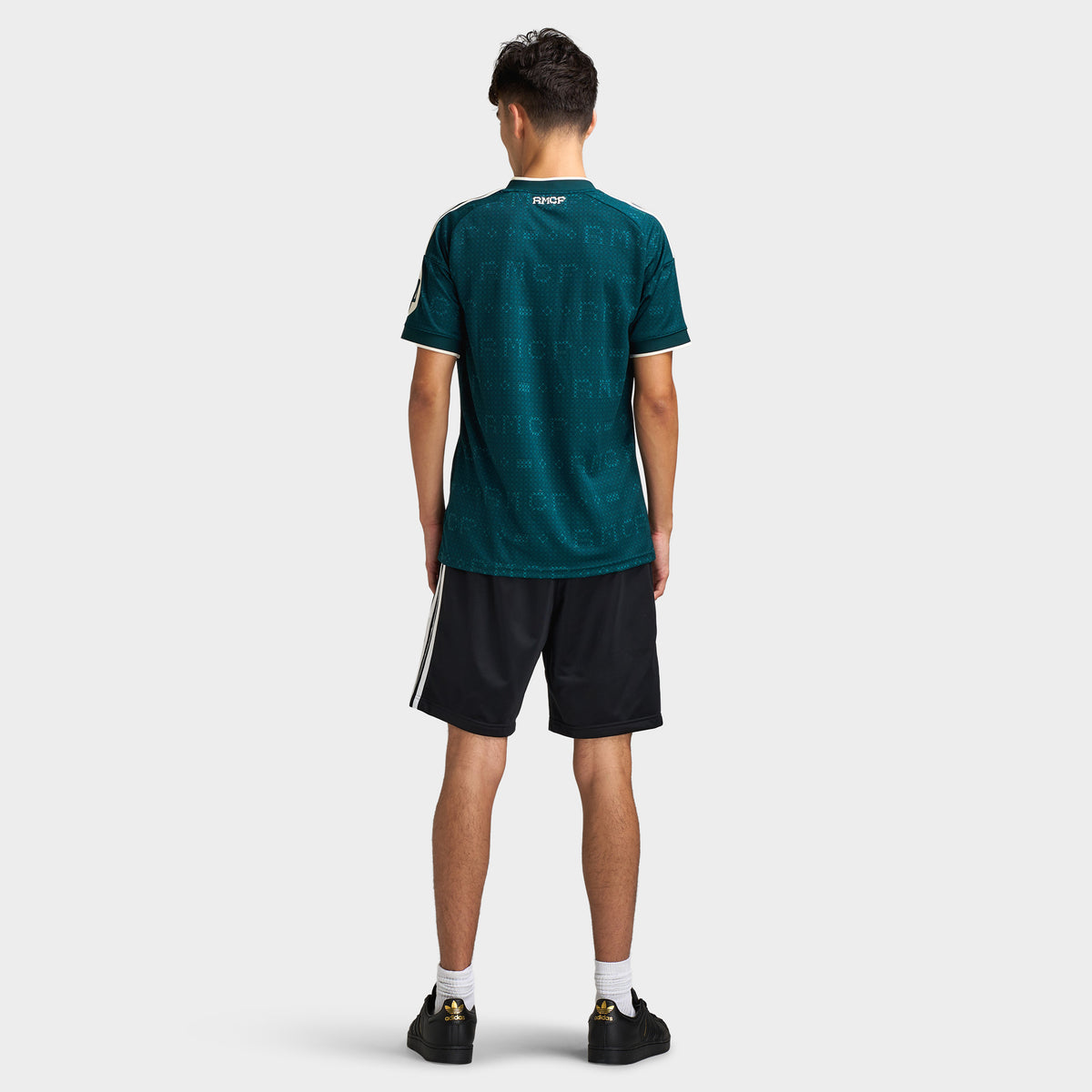 adidas Real Madrid Away Jersey. Full-body back view of model wearing aurora ivy soccer jersey with black shorts and dark shoes.