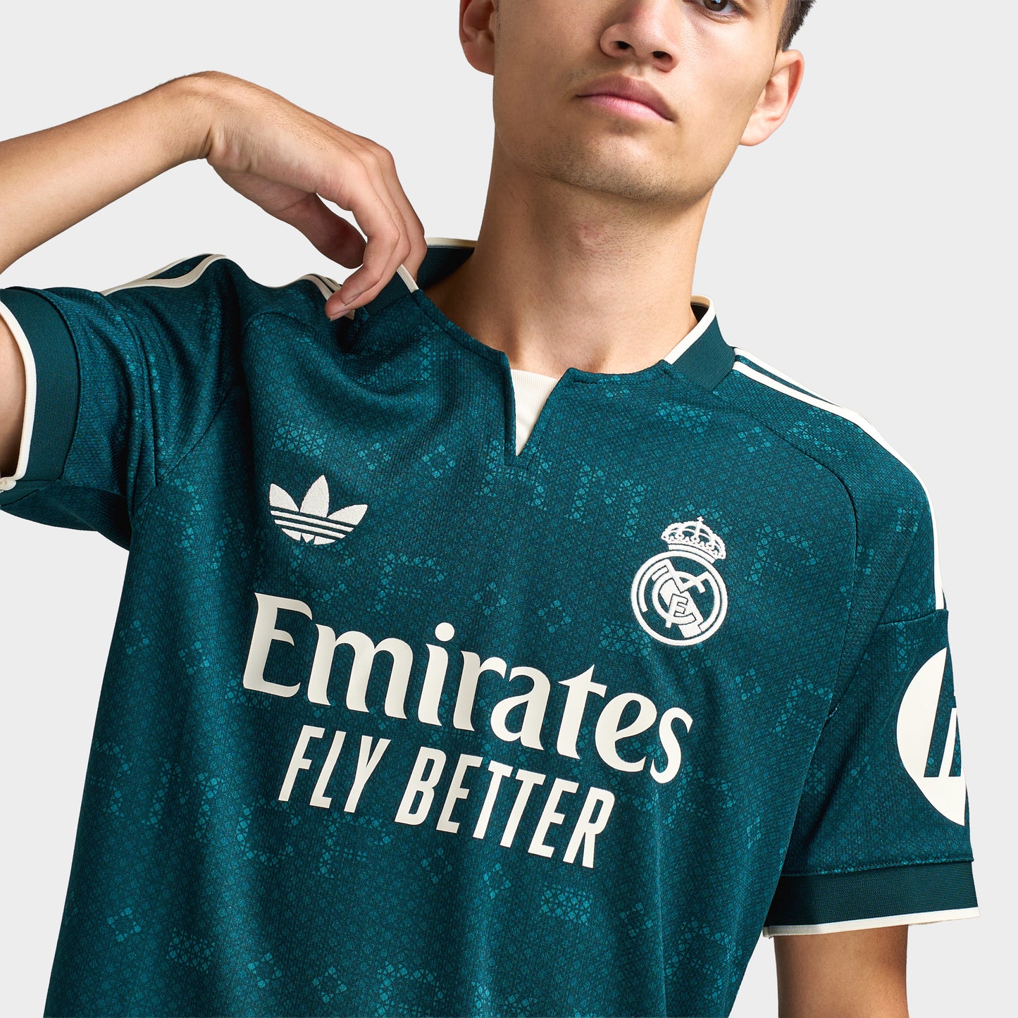 adidas Real Madrid Away Jersey. Close-up of aurora ivy soccer jersey showing the collar, adidas logo, Real Madrid crest and Emirates Fly Better sponsor graphic.