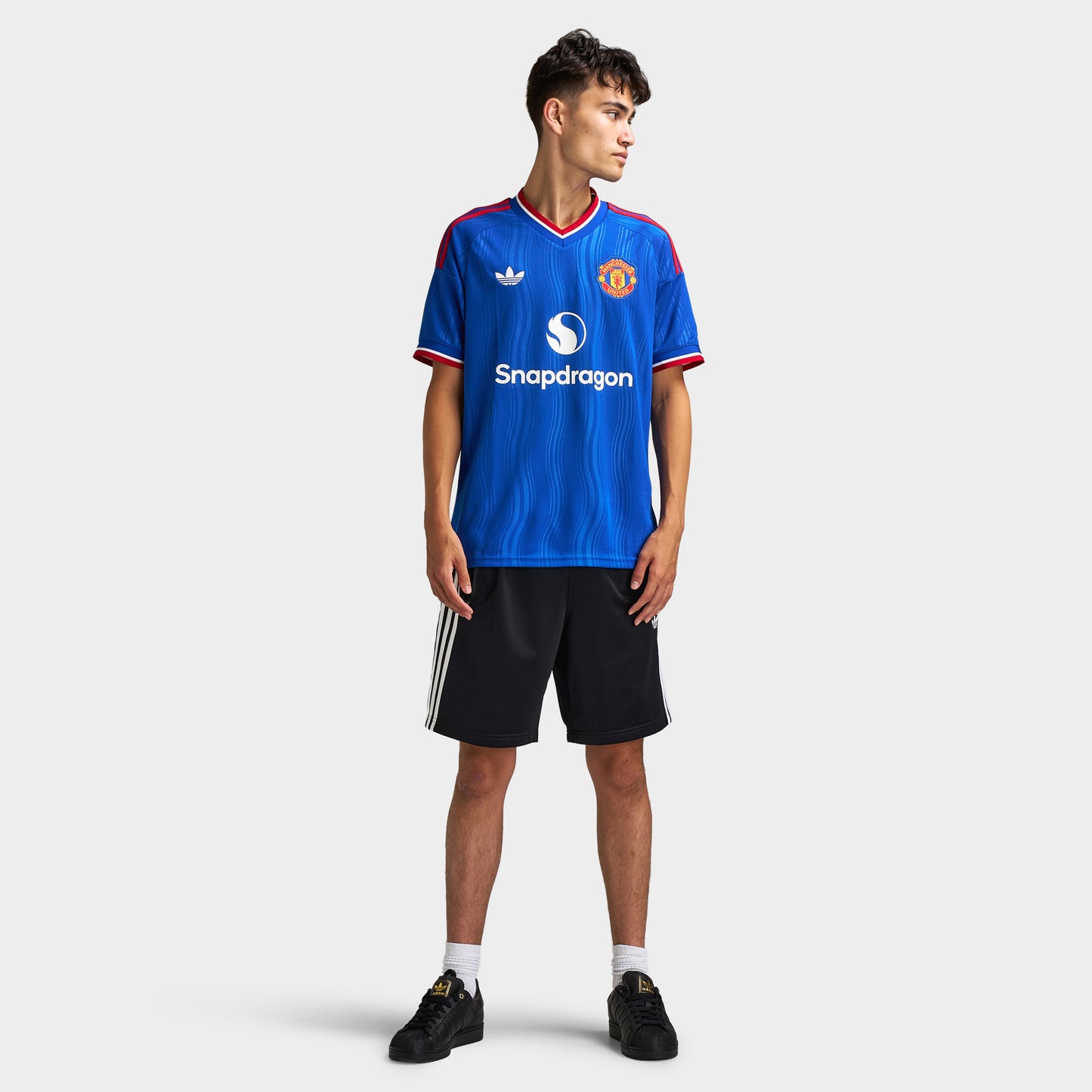adidas Manchester United Away Jersey. Full-body front view of model wearing team royal blue soccer jersey with black shorts and dark shoes.