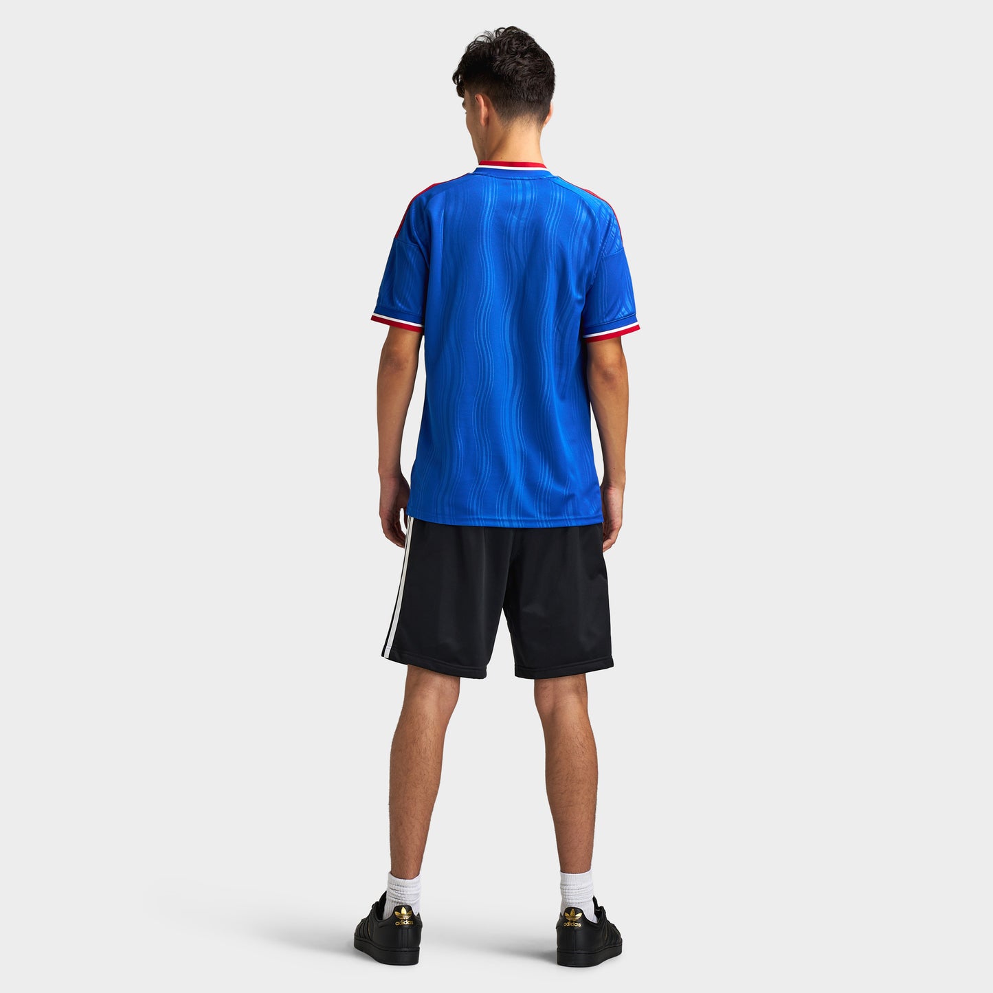 adidas Manchester United Away Jersey. Full-body back view of model wearing team royal blue soccer jersey with black shorts and dark shoes.