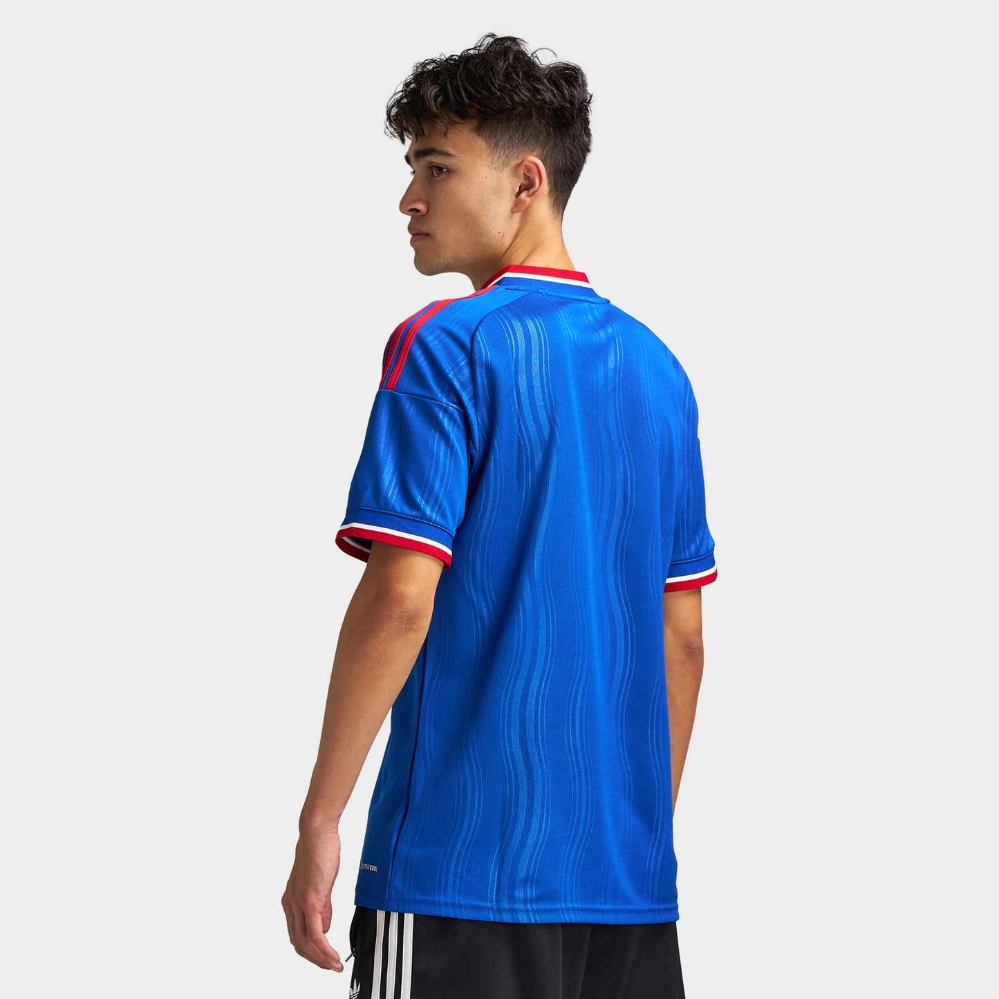 adidas Manchester United Away Jersey. Back three-quarter view of model wearing team royal blue soccer jersey with red trim and short sleeves.